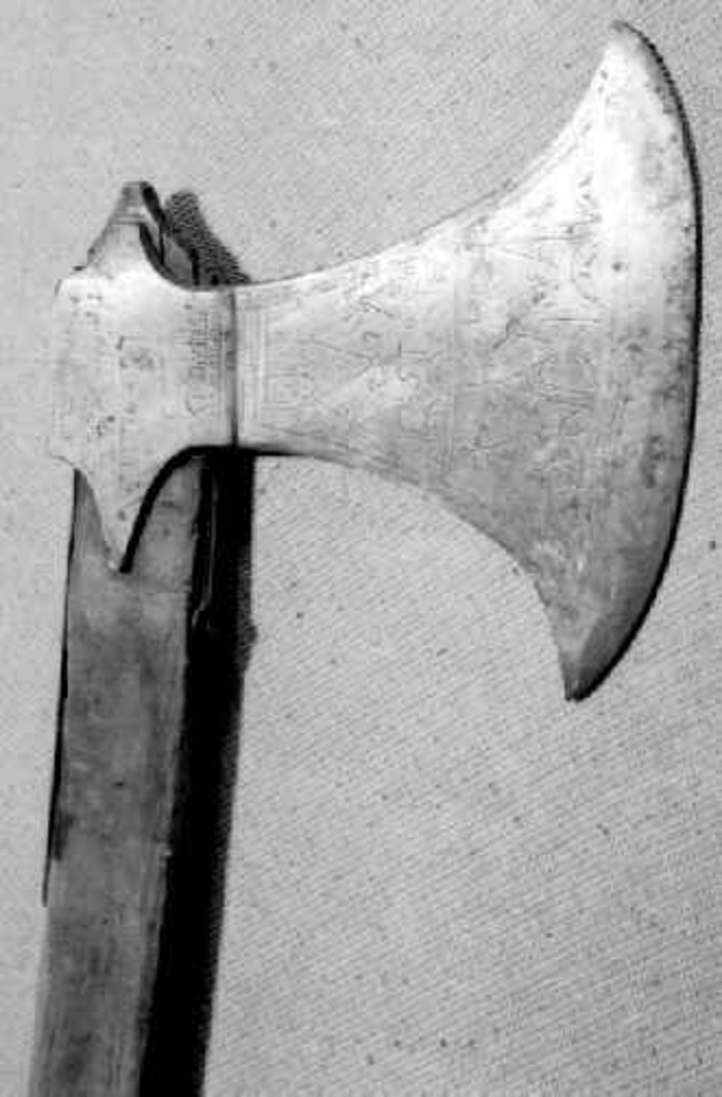 Symmetrisk blad. Bladet er tynt. 
Øsehammeren har skaftehull og fliker.
Etset dekor på begge sider. Stemplet TS på venstre side.
Gammelt treskaft med to orginale jernskinner med gravert dekor.
Jernskinnene er festet med nitter.