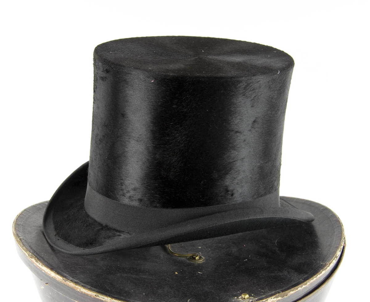 Sort flosshatt med sort ripsbånd og brun svettereim.  Det følger med en hatteeske.