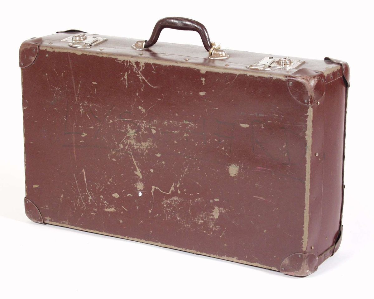 Kofferten er av brun papp og tre, kledd i blått papir innvendig. Håndtak, låser og hjørneforsterkere er av metall. Tekst er skrevet på koffertens langsider og papirlapper med tekst er klistret på koffertens kortsider.