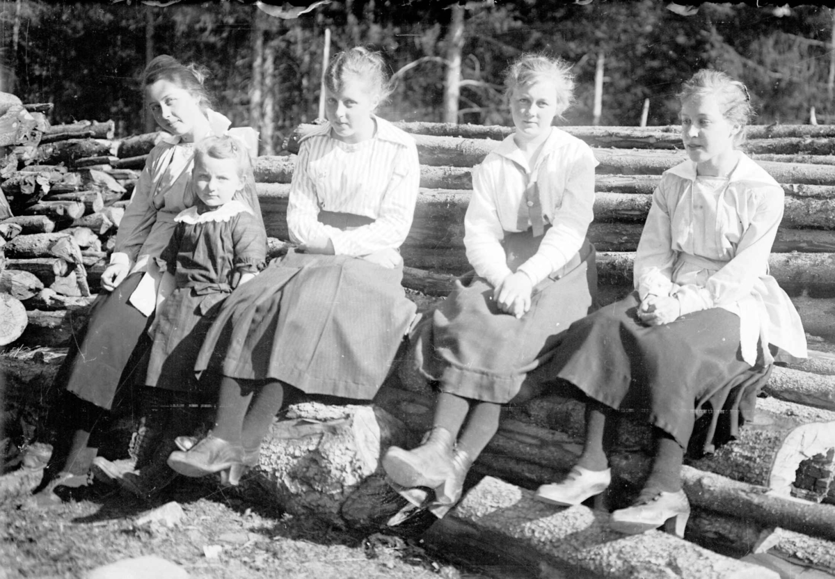 Fire unge kvinner og en liten pike som sitter på tømmer