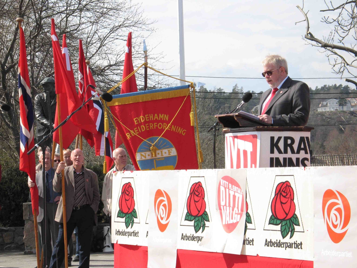 1.mai på Eydehavn. Talerstolen pyntet med rød rose motiv, med flaggborg og fane i bakgrunnen t.v. Dagens hovedtaler. 