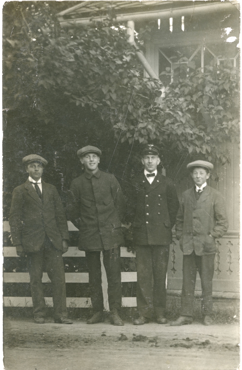 Fire unge menn, en i uniform står ved hage gjerde.