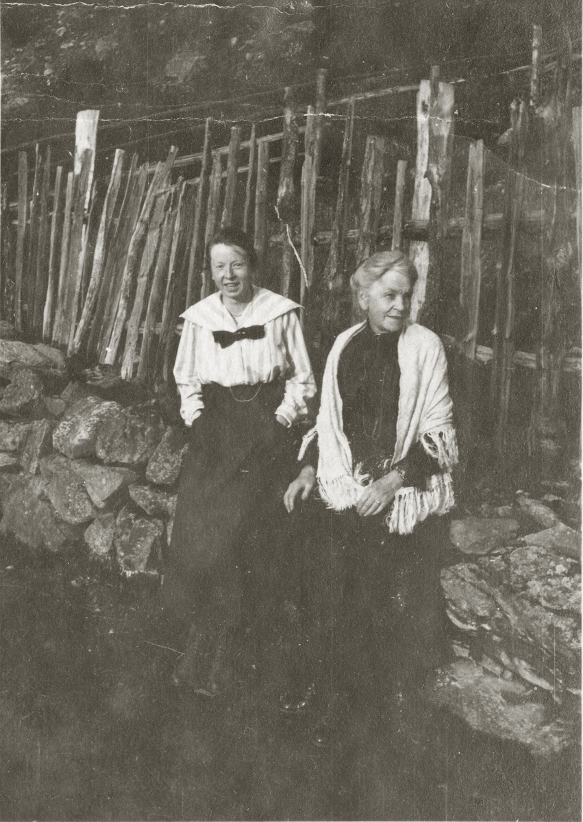 To damer sitter på steingjerde