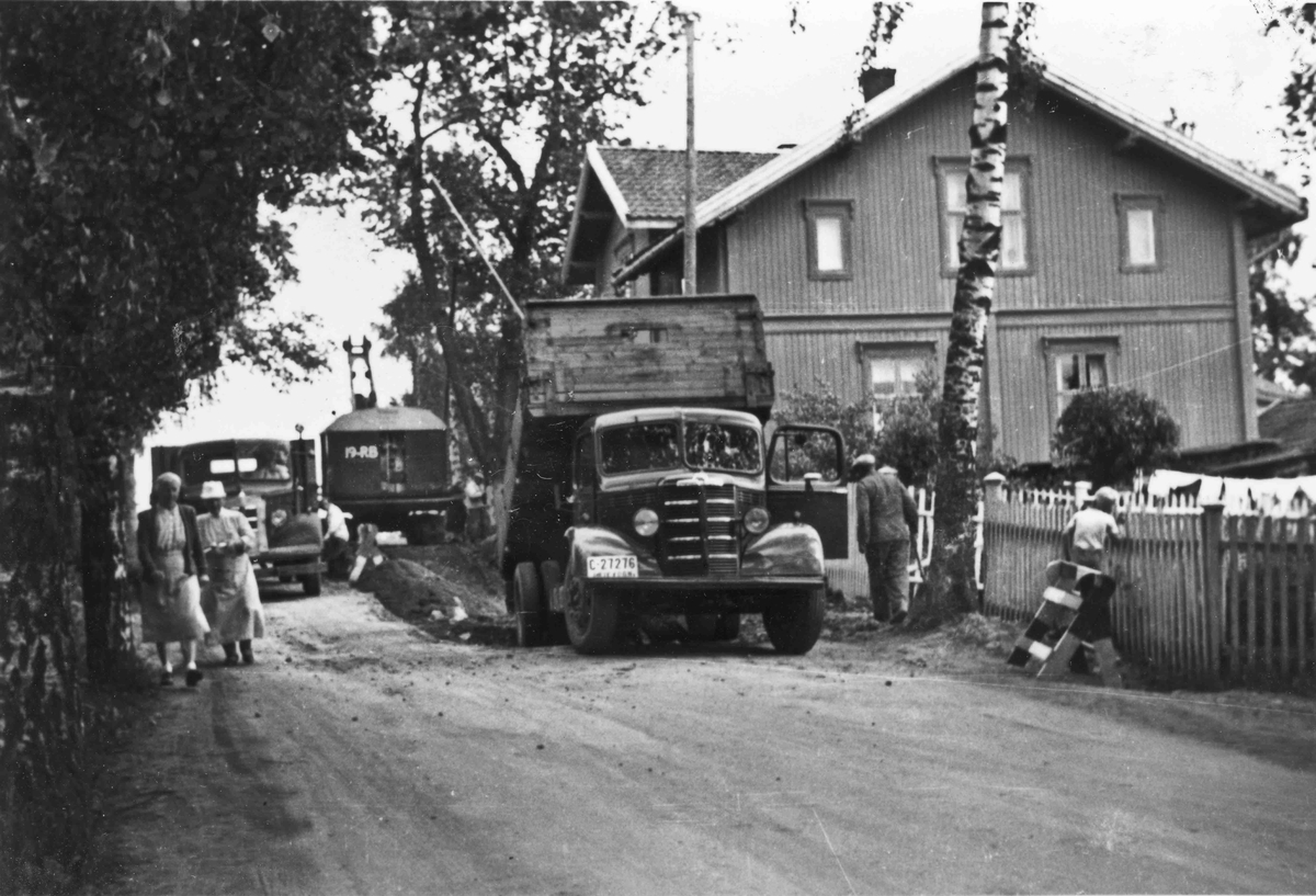Vegarbeid på Eidsvoll Verk. Bildet er tatt fra sør mot Pirotoppen. Dette var Trondheimsveien (Riksveg 50) til sist i året 1958, da den nye brua over Andelva ble tatt i bruk.
04.02.2014:
Nærmeste lastebil er en Bedford 1946-53-modell.
Skrevet av: Ivar E. Stav
