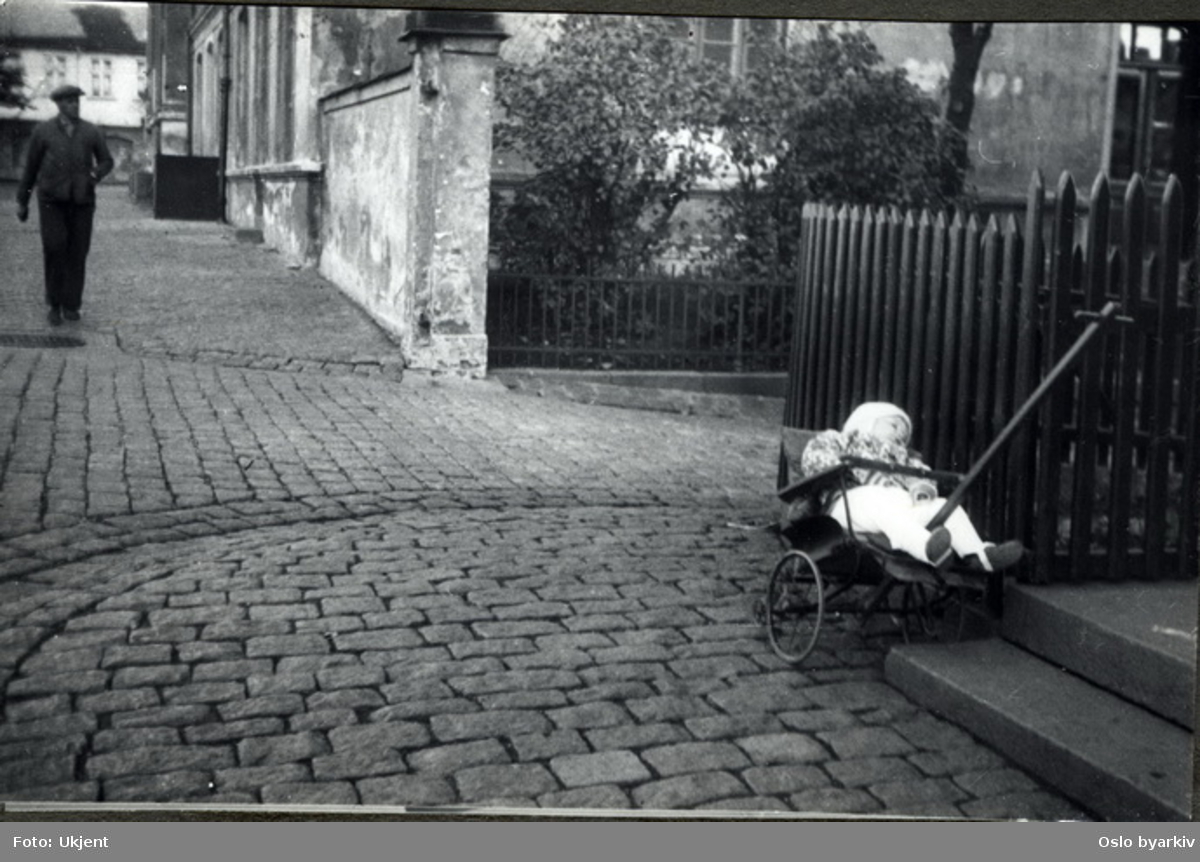 Lite barn som sover i en hjemmelaget trille / barnevogn i skolegården. Albumtittel: "Sofienberg skole femti år - første september 1933."