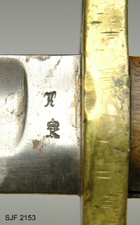 Sabelbajonett av type M/1860.  Våpenet har 57, 5 centimeter lang klinge, der den bakre delen er hulslipt i cirka 41 centimeters lengde på begge sider.  Her er klingen enegget.  Den fremre delen av sabelbajonetten er tveegget.  Bakerst på klingen oppunder parérplata, er det to K-er med kroner over (Kongsberg våpenfabrikks symbol) på den ene sida, og ei sifferrekke (8112) på den andre.  Grepet består av to treplater som er klinket mot tangen, mellom parérplata (foran) og et messingbeslag (bak) med spor for bajonettklakken (festing).  På den ene sida sitter det en fjærbelastet knapp som står i forbindelse med utløserklakken. Parérplata har et sirkelrundt hull med diameter på 1, 9 centimeter, som skulle tres inn på geværpipa.  I enden av det nevnte endebeslaget på grepet er det et gjennombrutt hull med en lærstropp. 

Sabelbajonetter av denne typen ble brukt til firelinjers kort kammerladingsgevær (M/1860).  Denne bajonettypen er en variant av M/1859, som ble konstruert for 15-lødig tappstusser, 18-lødig kammerladingsgevær og avkortete kammerladingsgevær.  Diametrene på slike våpen var noe større enn på kammerladingsgevær M/1860, og dimensjoneringa av parérplatene ble følgelig noe ulike på de to nevnte utgavene av sabelbajonetten fra Kongsberg våpenfabrikk. Dette var for øvrig de første bajonettypene som kunne festes under geværpipa, noe som ble mulig da det kom geværtyper som ikke hadde ladestokk.  På eldre militære geværer ble bajonettene plassert på den ene side av geværpipa, noe som skal ha medført at skuddene hadde en tendens til å trekkes noe sidevegs i forhold til de målene skytterne siktet mot.  Denne bajonettypen ble tilgjengelig omkring 1860, i første omgang for infanteriavdelingene, etter hvert også for artillerister.  I tillegg til de to nevnte sabelbajonettene ble det også produsert en noe mindre variant av denne sabelbajonetten til bruk på Krigsskolens kammerladingsgeværer. 

Bajonetten har tilhørt Kolbein Helstad, Gjesåsen. 