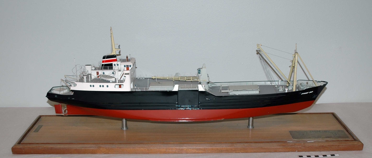 Modell av en motorbåt med lasterom, bom, vinsj og kran ved front. Festet på en plate av treverk.