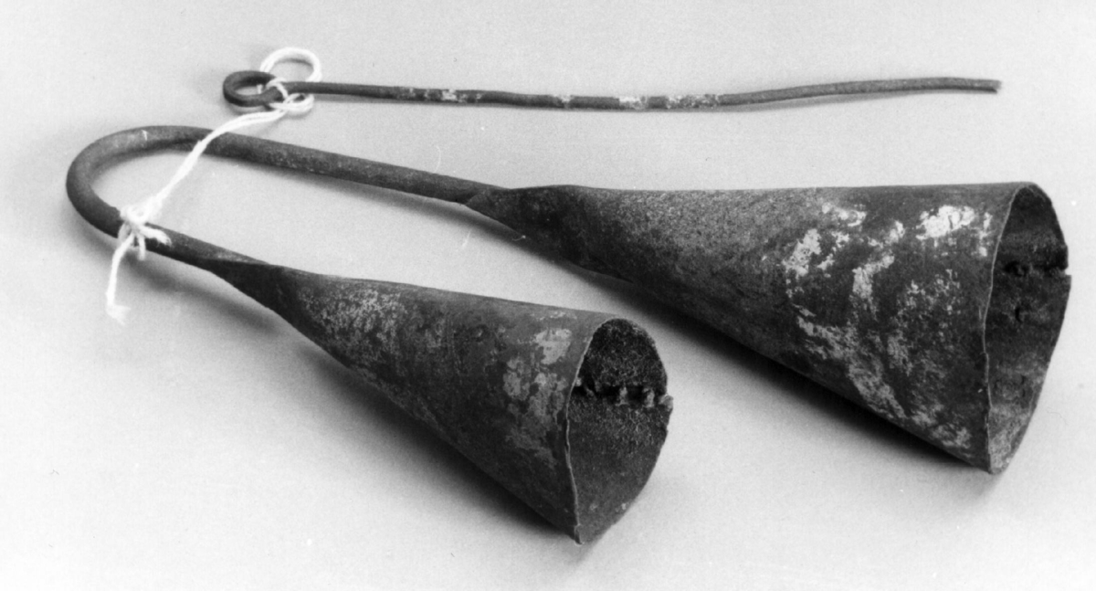 To koniske klokker av smidd jern, forskjellig størelse, forbundet ved en påloddet jernbøyle. Slås med en smal jernstikke.

