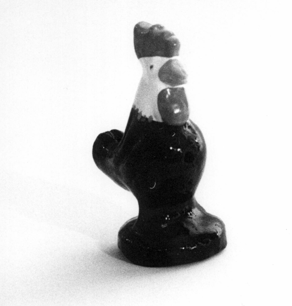 Spaltefløyte i keramikk i form av en hane på en rund sokkel. Utvendig glasert: kam, pose og nebb rød, hode hvitt, korpus og sokkel svart.
Spalte og labium i stjerten.
Ett fingerhull.

