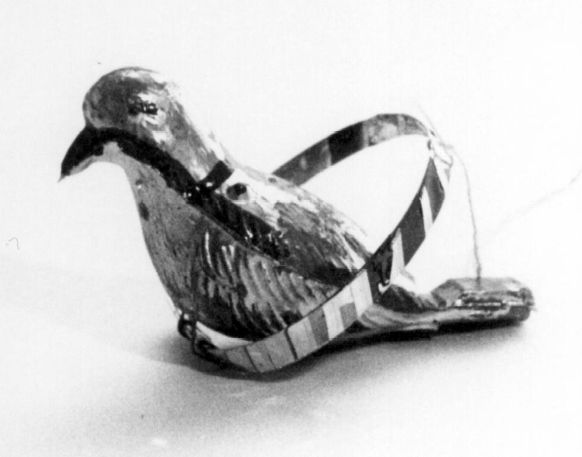 Spaltefløyte. Barneleke i form av plastfugl med spalte og blåsekant i stjerten. Fuglen er utvendig dekorert med sølvfarget og rød maling og sitter på en papirbelagt plastring.