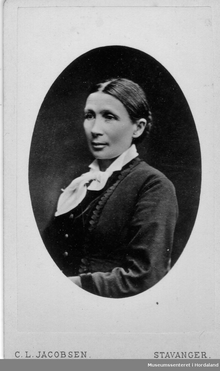Kvinne med midtskill, håret samla i nakken, kvit sløyfe i halsen og jakke
