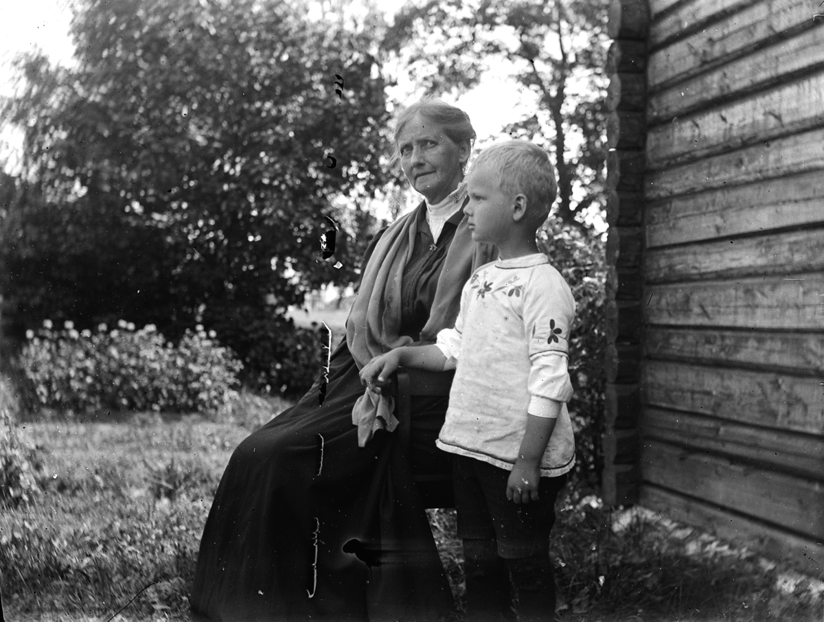 Kvinne med barnebarn i husveggen i Kvalstua, Helgøya. Anne (Eliesson) Dybwad og Wilhelm Dybwad.