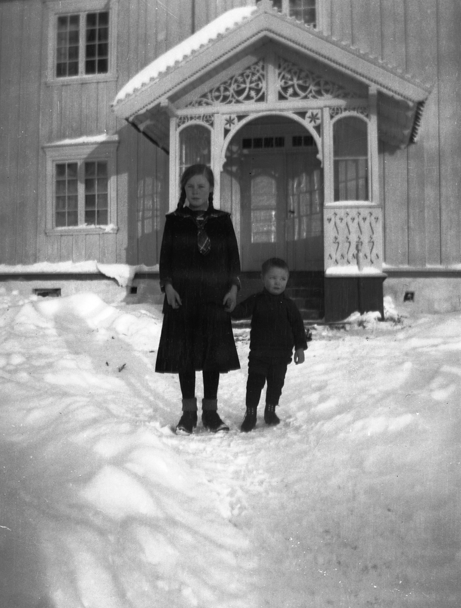 Gutt og jente i snøen foran veranda, vinter. 