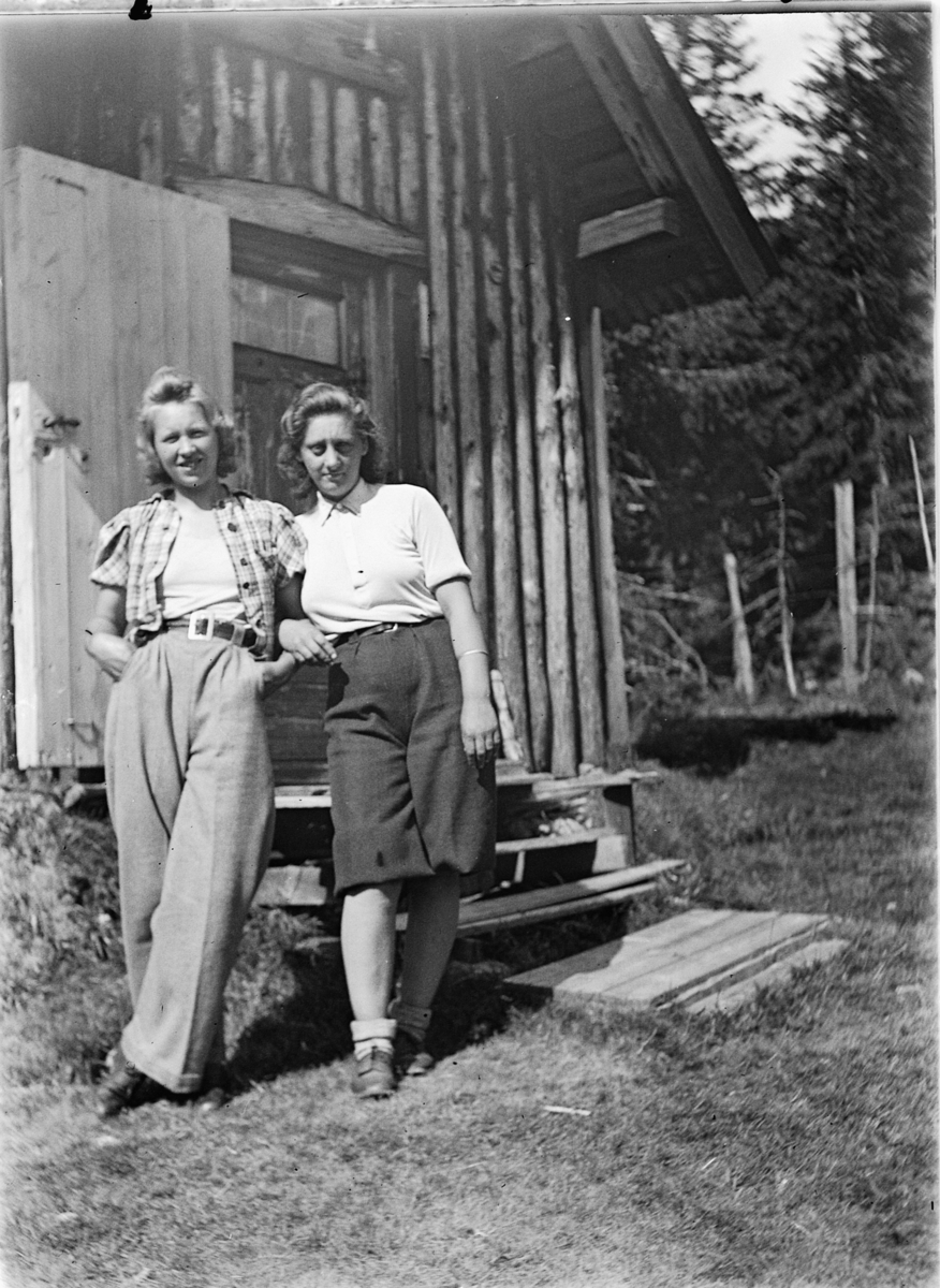 To kvinner utenfor ei hytte. 