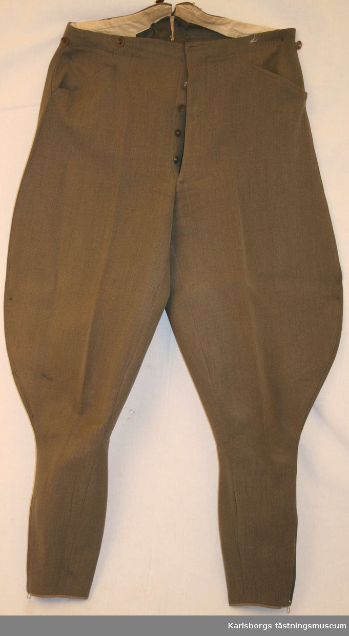 Ridbyxa m/1939 av gråbrungrön komiss. Två snedställda sidfickor en bakficka med en knapp. Dragkjedjor i byxbenens nederkanter.