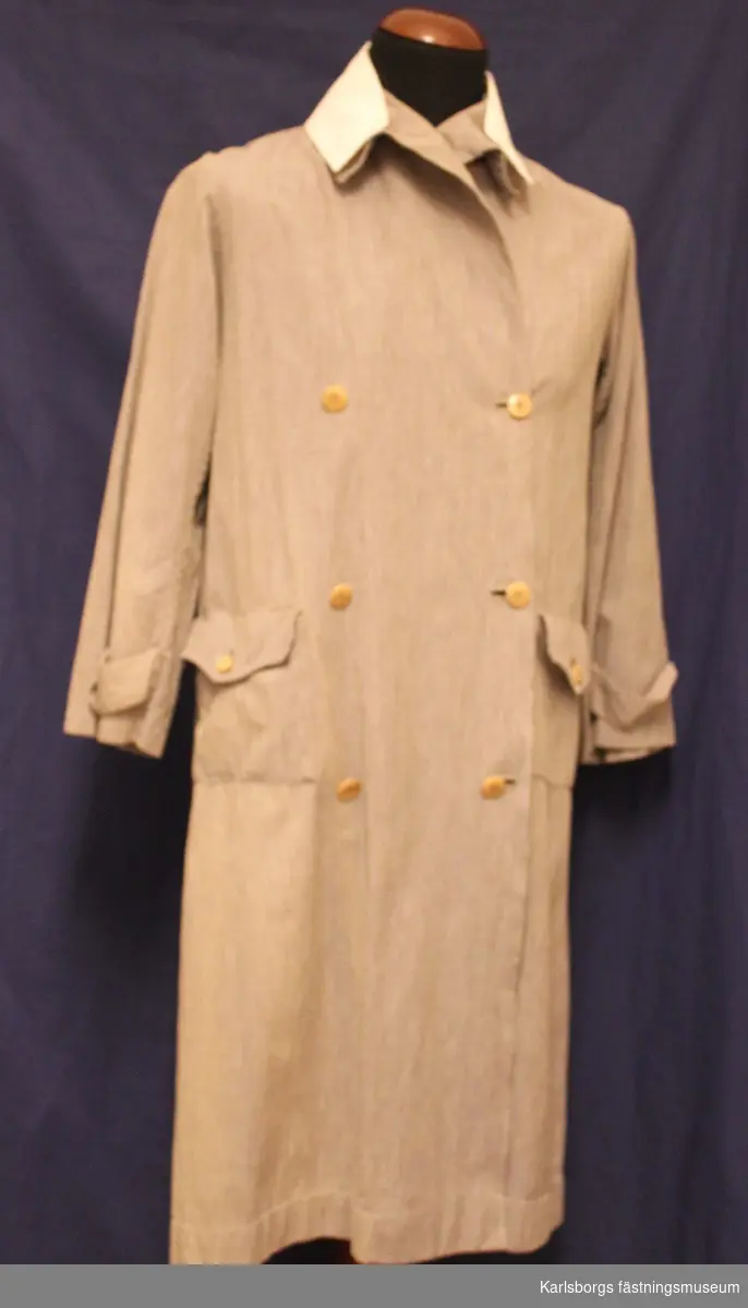 Rockklänning för armélotta m/1923. Dubbelknäppt fram, utanpåsydda sidfickor med lock o knapp. Vit påknäppbar krage samt manschetter.