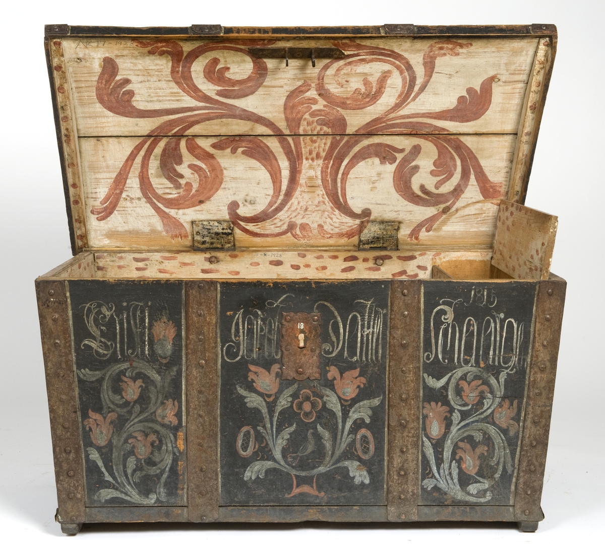 Kiste med buet lokk og smijernsbeslag og bånd. Rosemalt lokk og tre sider. innvnedig bemalt og med leddik. Kisten har små føtter.