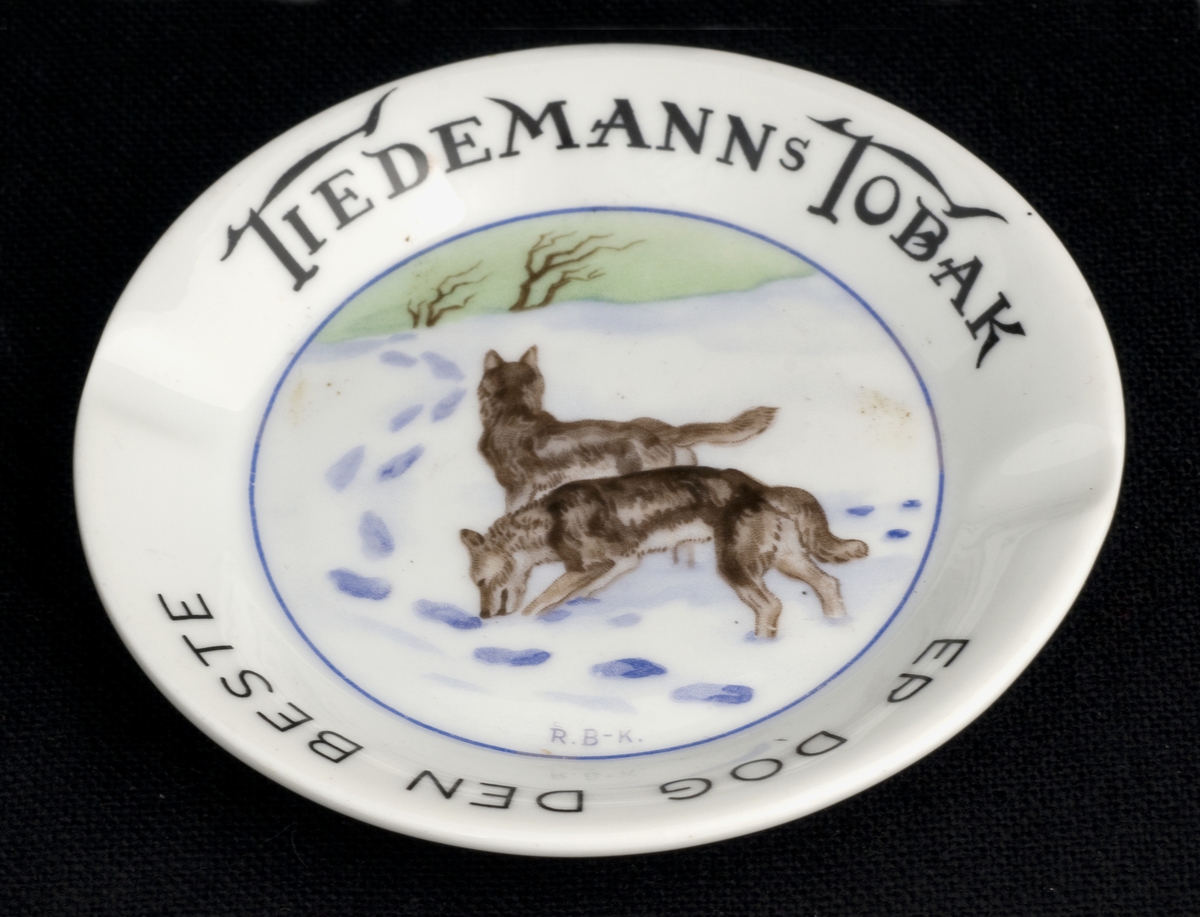 Lite, rundt askebeger i porselen med to fordypninger i randen. Påtrykket motiv av to ulver etter original av Halfdan Gran.