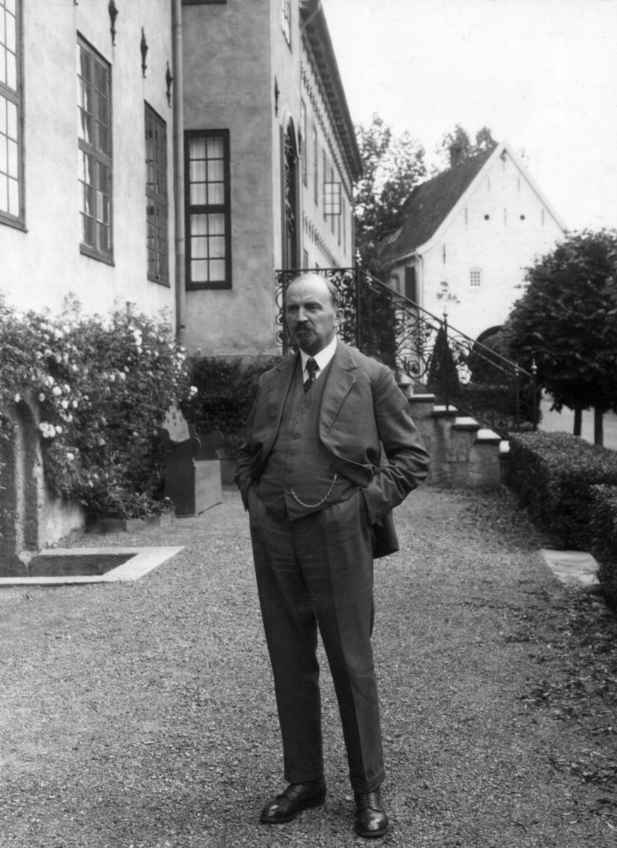 Direktør Hans Aall  stående med roser i bakgrunnen, foran Bybygningen, bygning nr. 311.