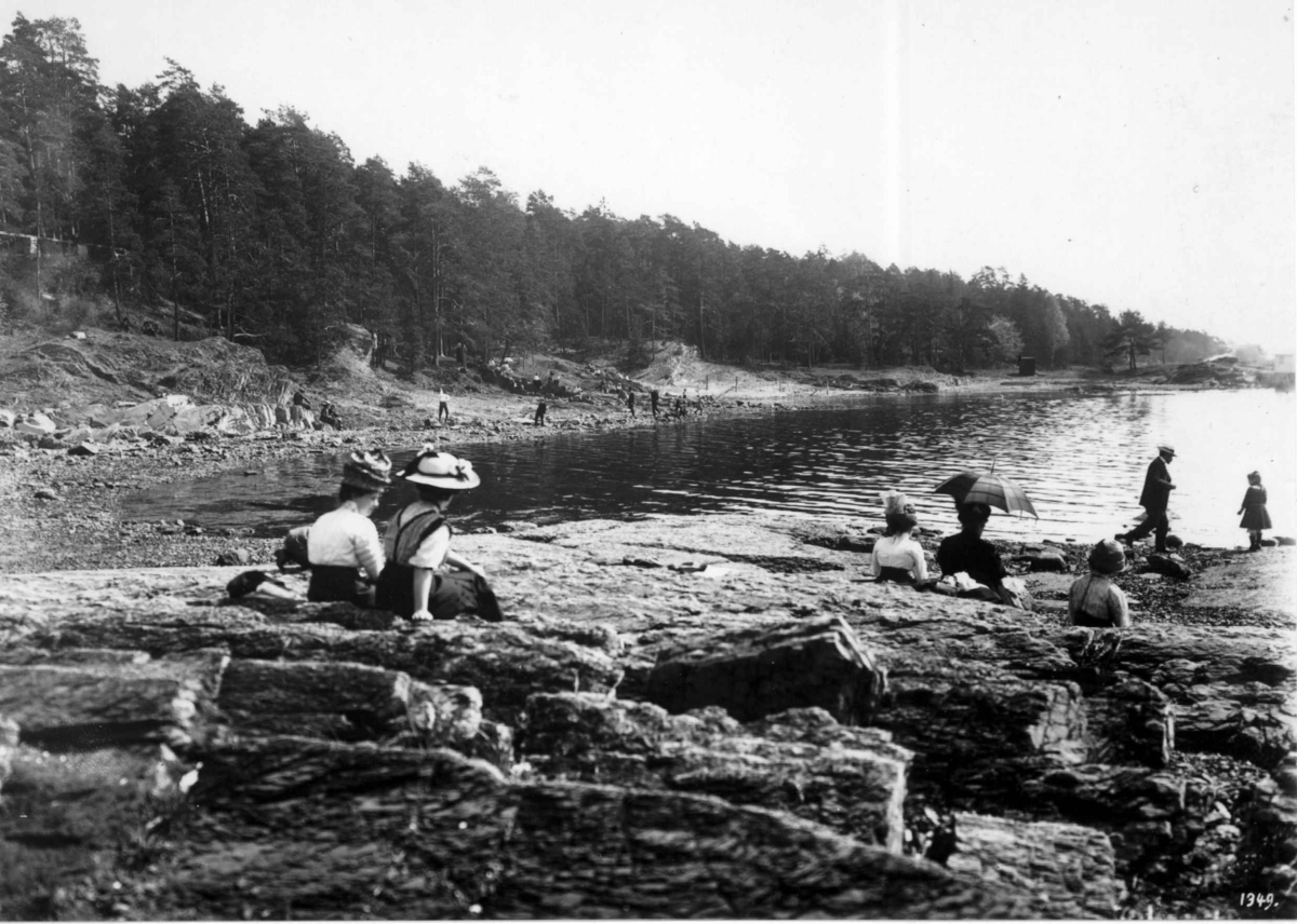 Bygdøy, Oslo 1905. Sommerliv. Mennesker på stranden, antatt Paradisbukta. Mennene i dress.  Kvinnene i lange
kjoler eller skjørt. Alle med hatter.